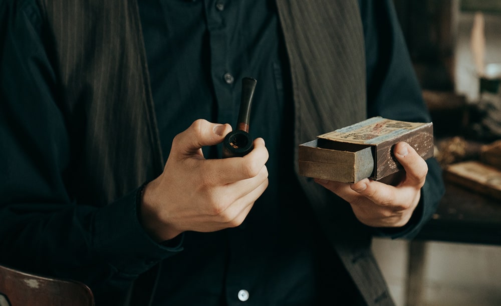 muž drží fajku na tabak a krabičku s fajkovým tabakom