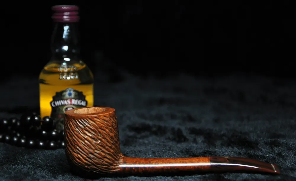 Briarová fajka na tabak položená na tmavom pozadí s malou fľaškou Chivas regal whisky