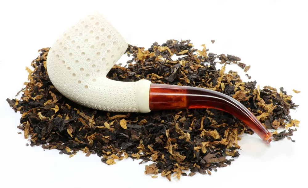 Fajka na tabak z morskej peny s akrylovým náustkom na kôpke rozsypaného tabaku