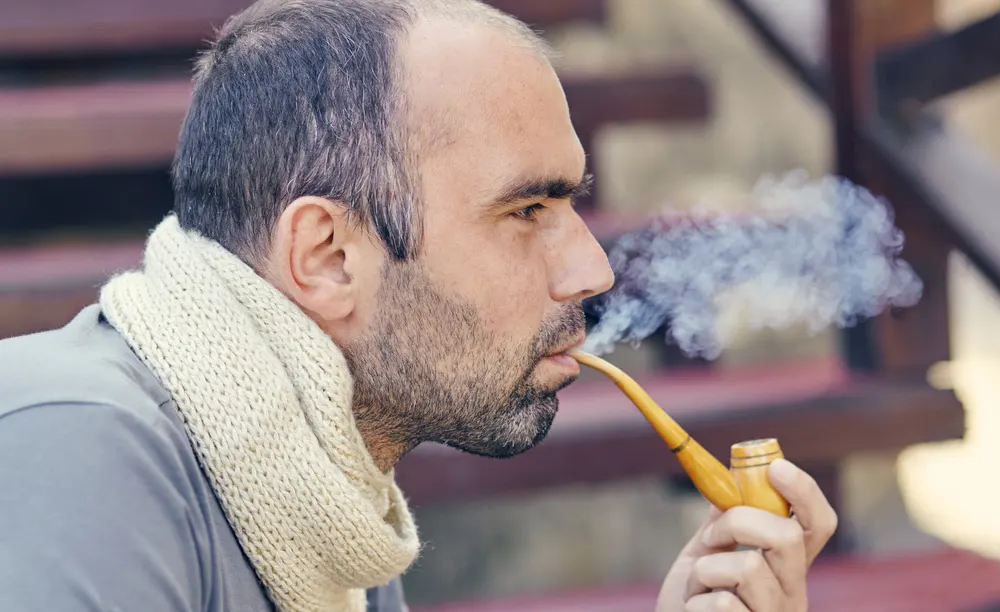 Muž s bielym pleteným šalóm fajčí fajku - pohľad z profilu