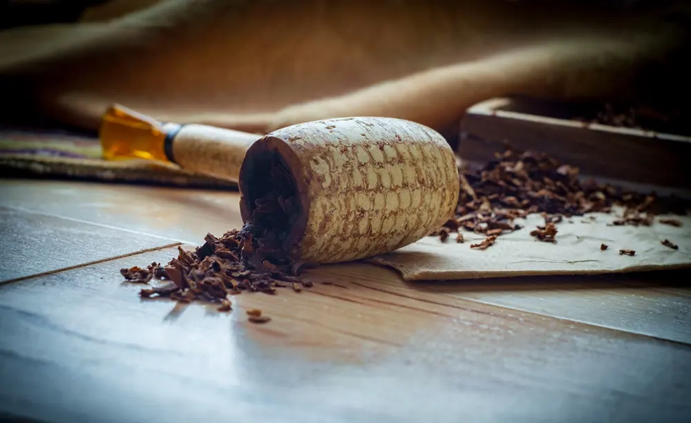 Fajka na tabak vyrobená z kukuričného klasu, rozsypaný fajkový tabak na štylizovanom pozadí
