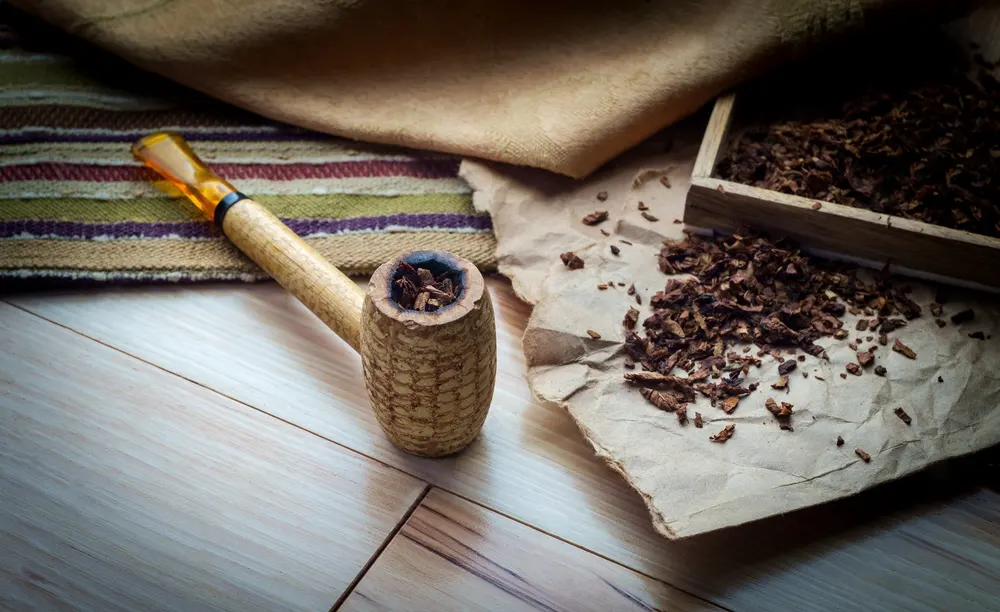 Fajka na tabak vyrobená z kukuričného klasu, rozsypaný fajkový tabak na štylizovanom pozadí