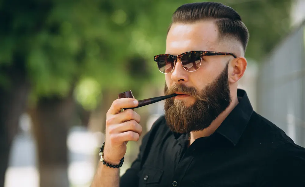 Muž v slnečných okuliaroch fajčí fajku na tabak